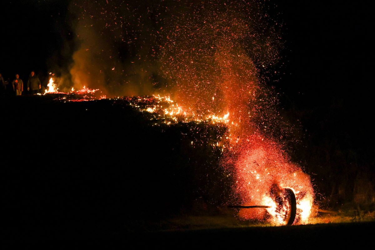 A wooden Easter wheel, filled with straw, rolls down a hillside ablaze during the Easter wheel race, leaving a long trail of fire in its wake.