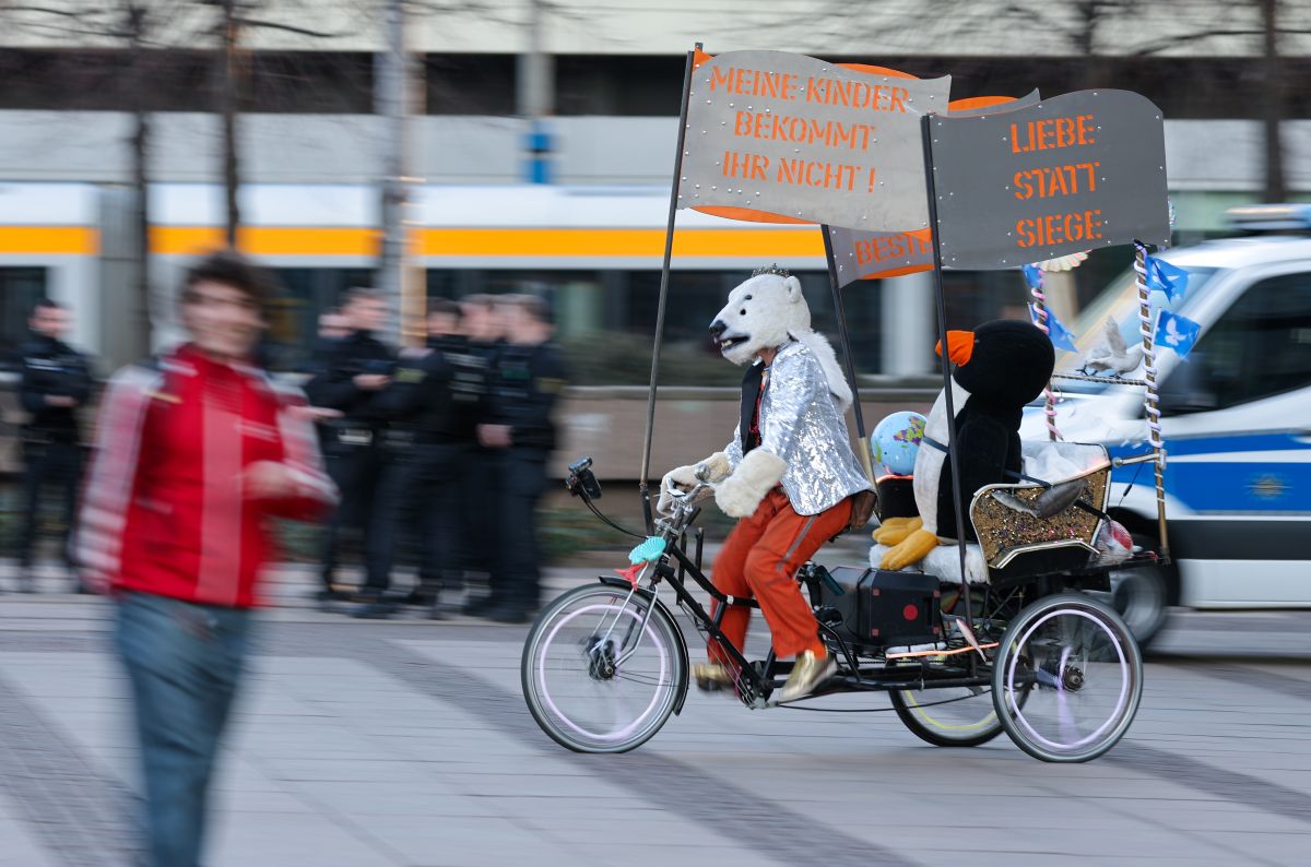 A person in a polar bear mask rides a tricycle with protest signs against military conscription.