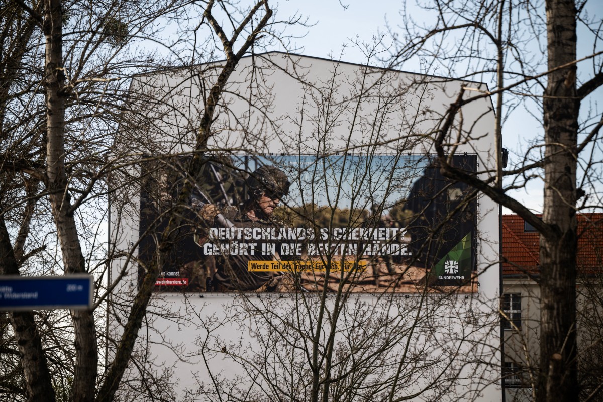 A german army recruitment poster is seen on a warehouse through the trees.
