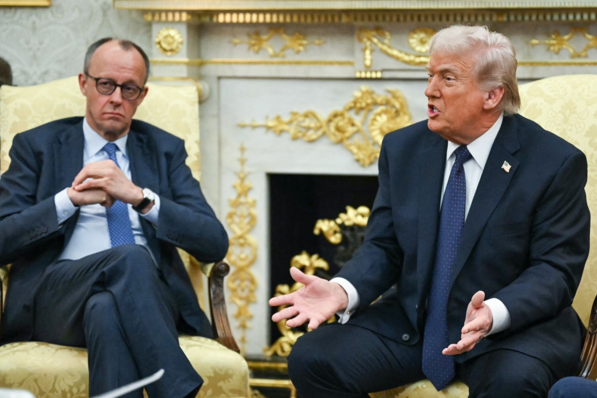 Merz holds his hands quietly while Trump speaks and gestures in a gold-adorned oval office.