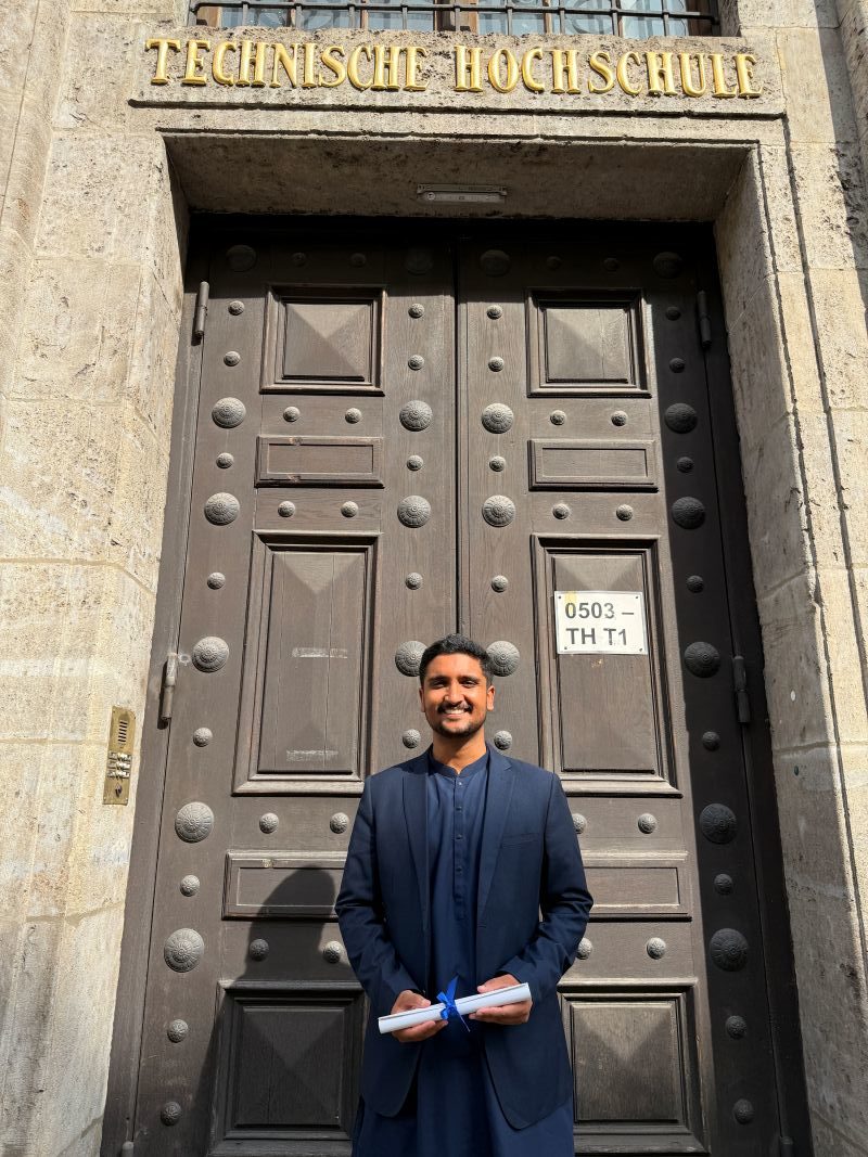 Saad Arshard stands in front of the doors of a technical university in his graduation attire.
