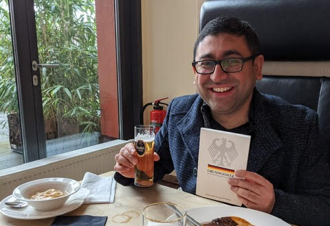 Mihir Nayak holds the Grundgesetz document and a beer after becoming German. 