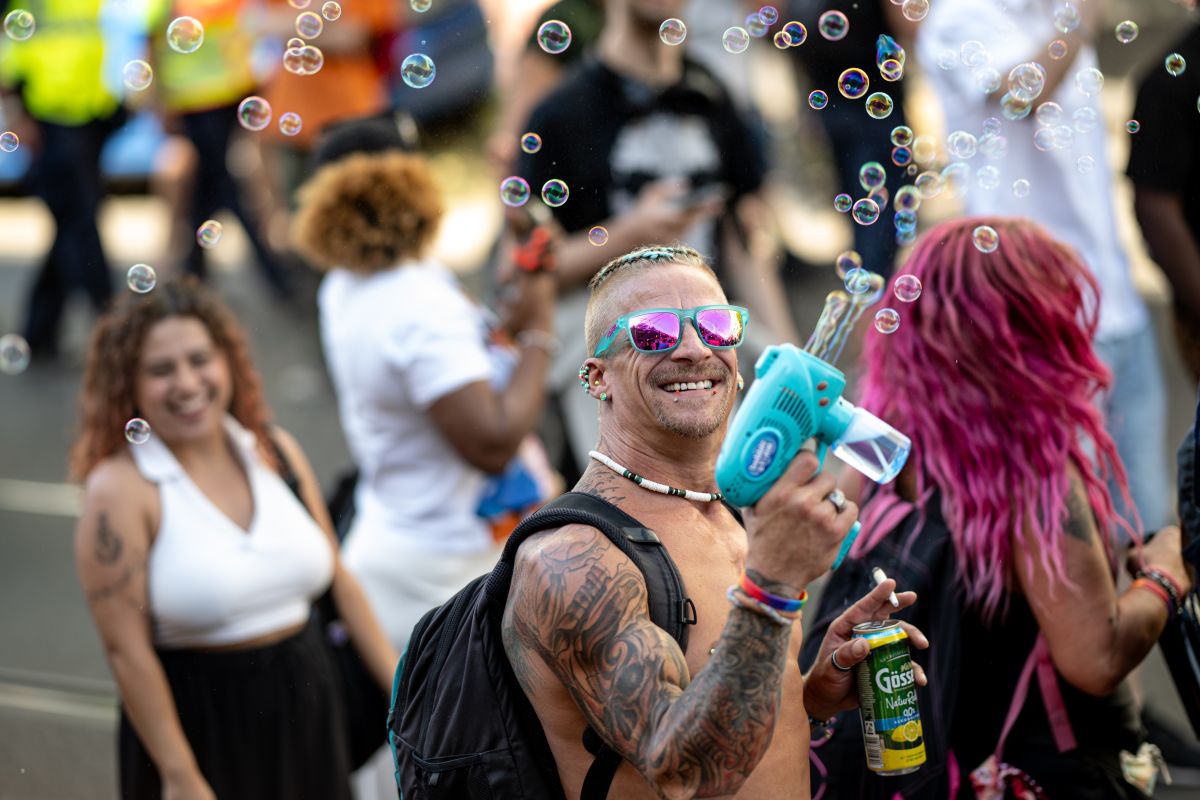 A man with cool sunglasses shoots a bubble gun in the sky.