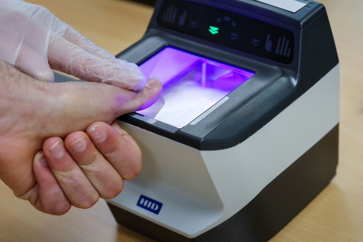 A man's thumb is held onto a fingerprint scanner.
