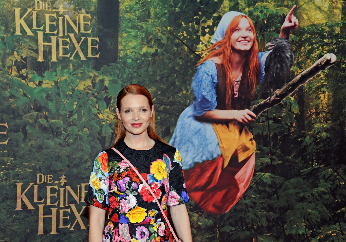 A woman stands in front of a poster of a witch on a broomstick