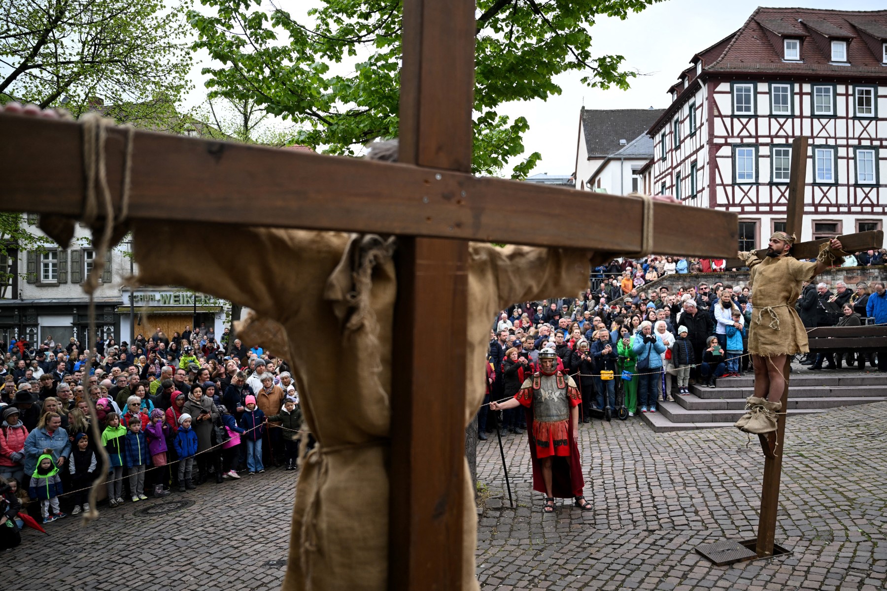Two men dressed as peasants are strapped to crosses in front of a large crowd of on-lookers.