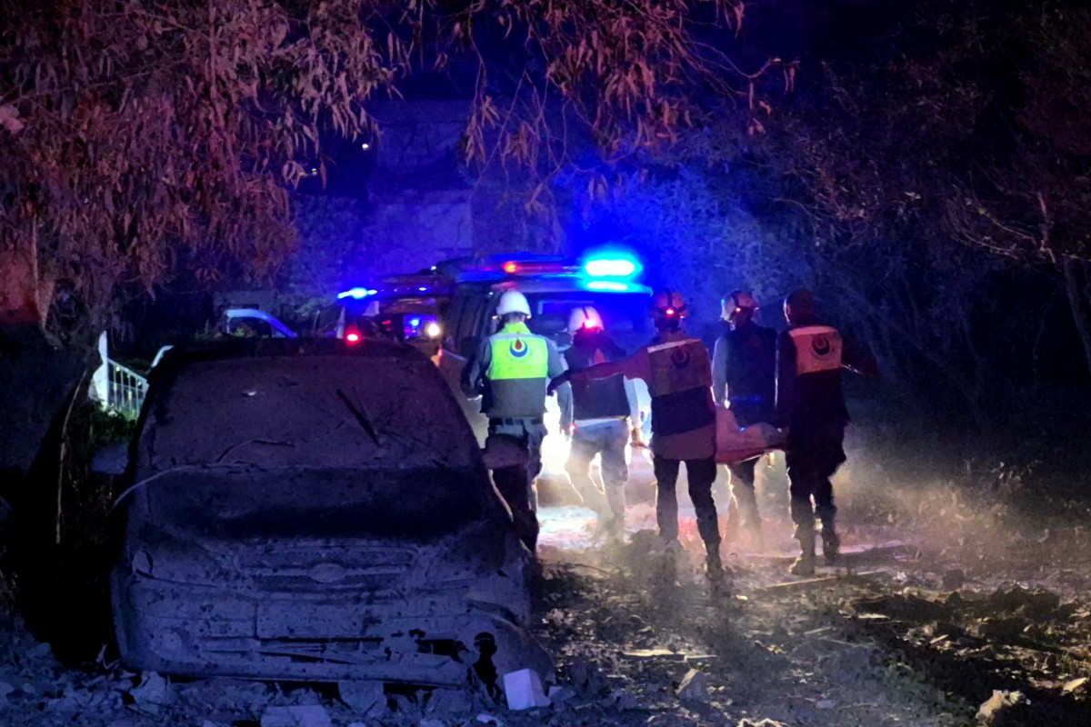 First responders are seen carrying a stretcher down a street covered in ash and rubble.