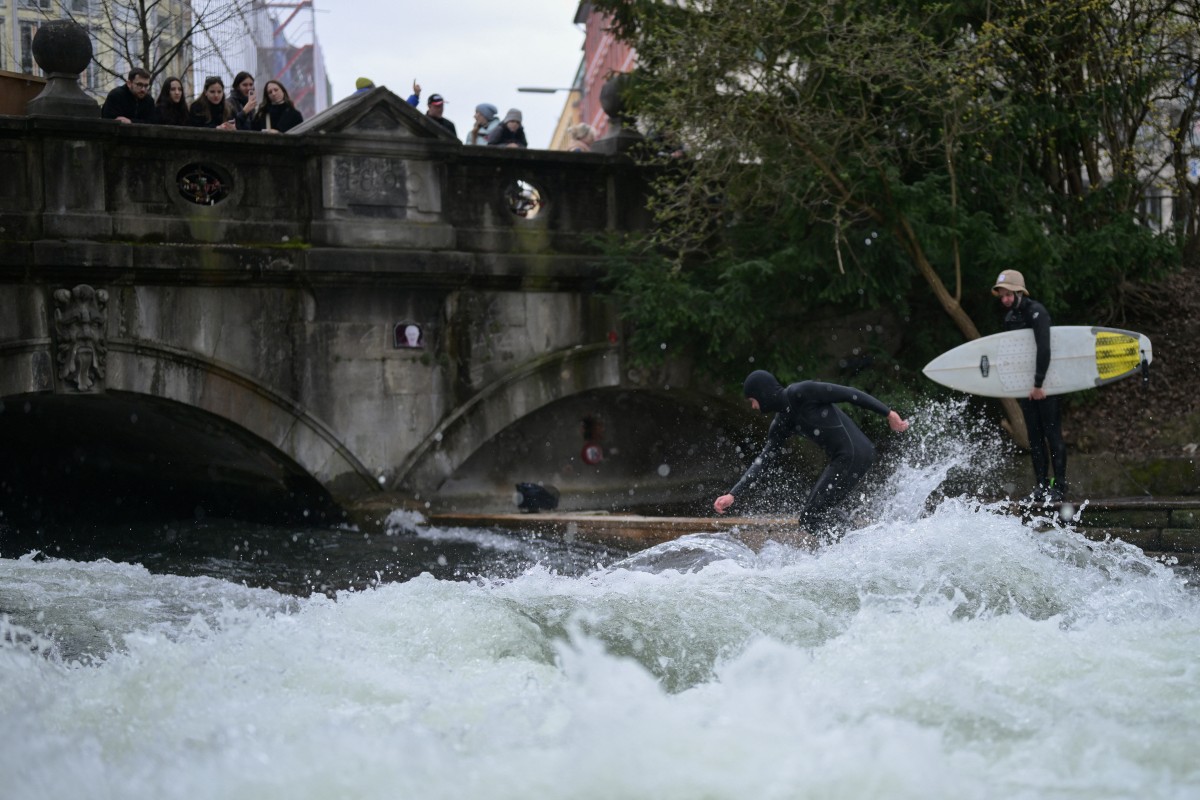 A surfer hops into a wave on the Isar river in Munich as spectators look on.