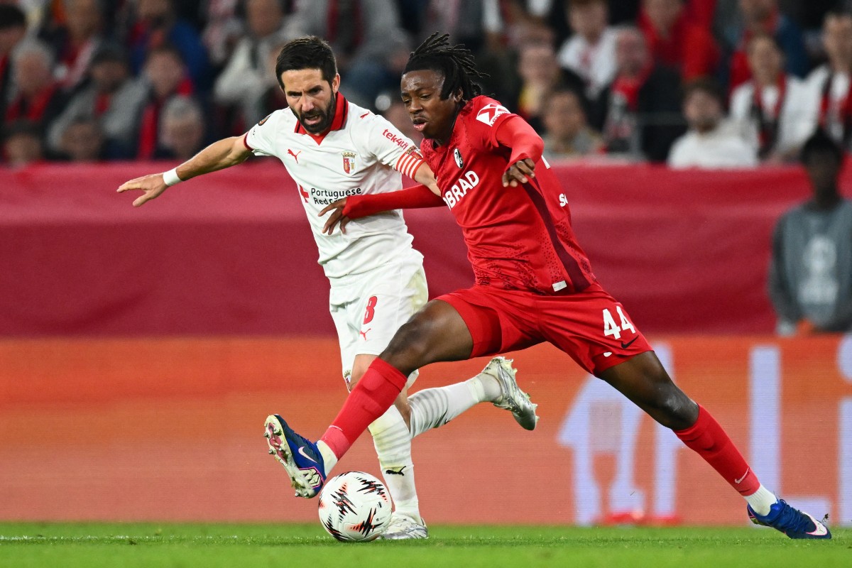 A Freiburg player in red jumps on the ball ahead of a Braga player in white.