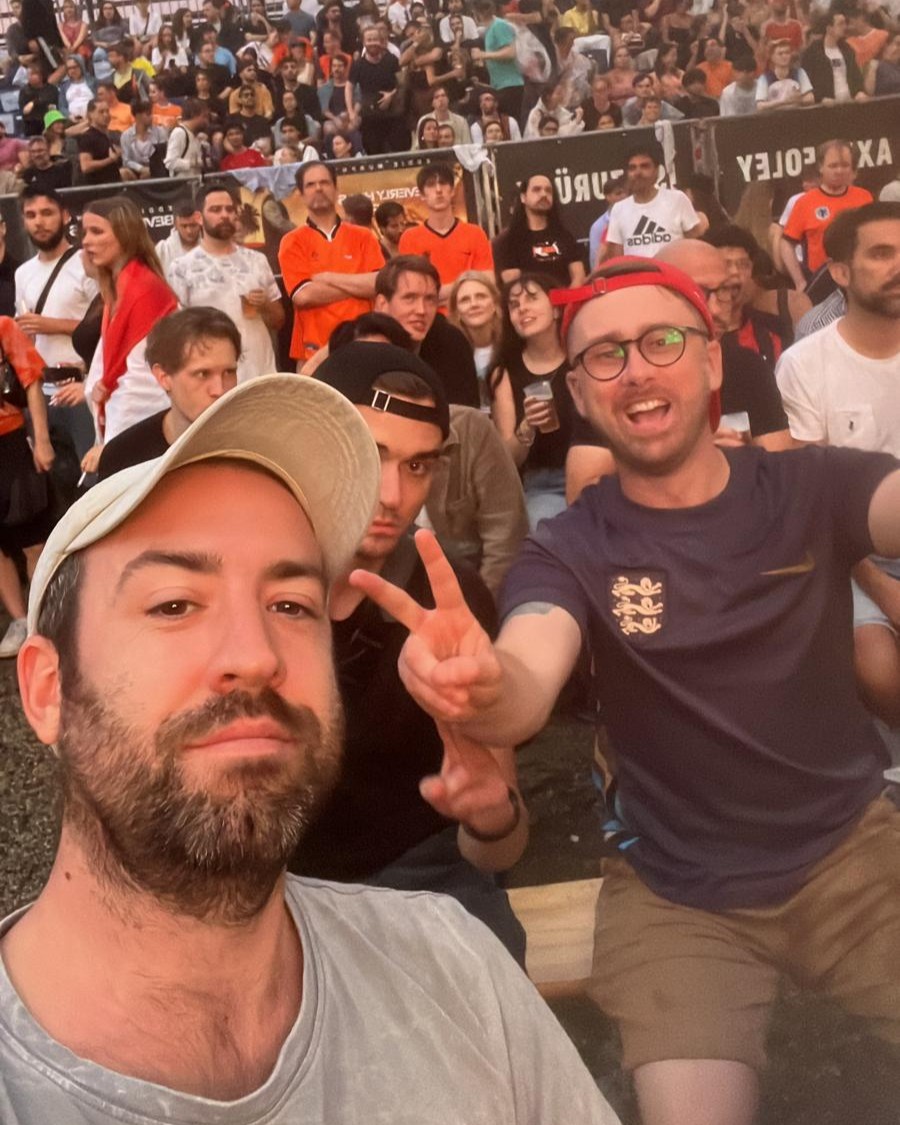 Shane takes a selfie in front of a crowd of football fans wearing oragne.