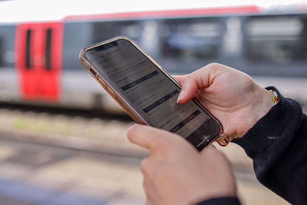 a woman looks at her phone with a train in the background