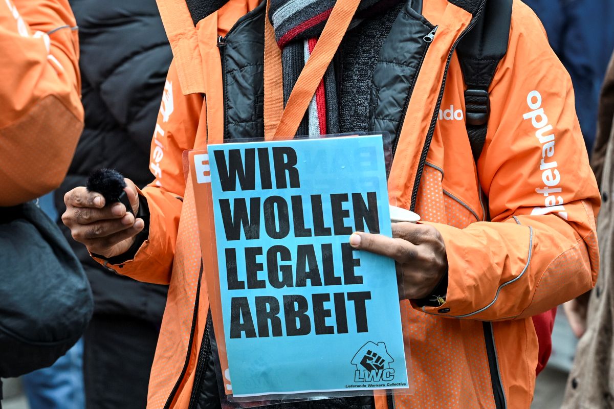 A lieferando rider hols a protest sign that says 'we want legal work'.