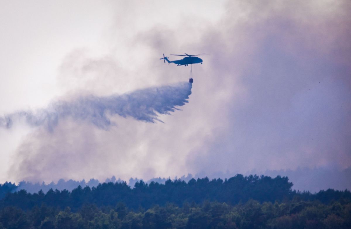 A helicopter dumps a large stream of water over an area of forest where a fire had recently burned.