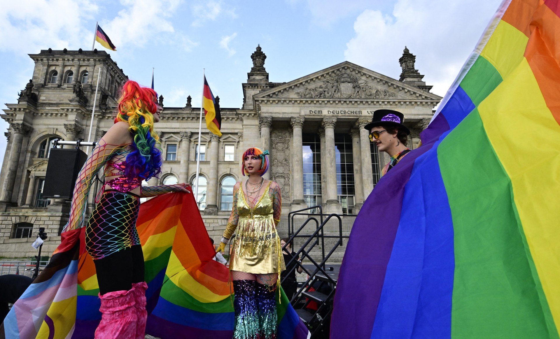 Performers on stilts pose with an Inter* Inclusive Pride Flag (L) and a rainbow flag (R) in front of the Reichstag building that houses the Bundestag (lower house of Parliament) on the eve of the 2025 Berlin Christopher Street Day in Berlin