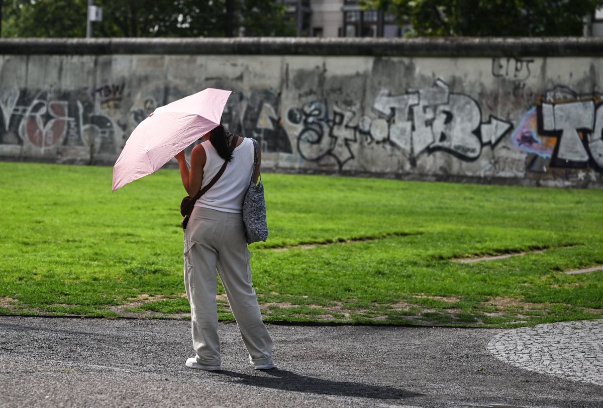 A woman with a pink umbrella looks at a section of Berlin wall