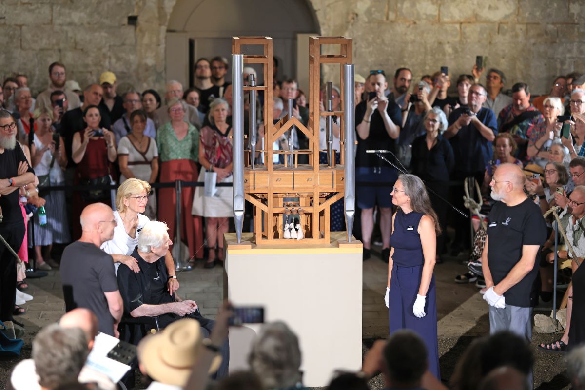men and women stand in a wide circle around a wooden object