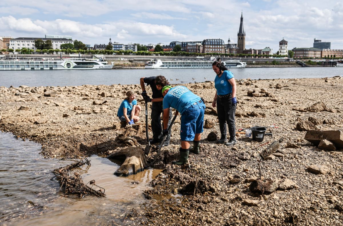 men and women in blue t-shirts use shovels to remove a tyre from mud