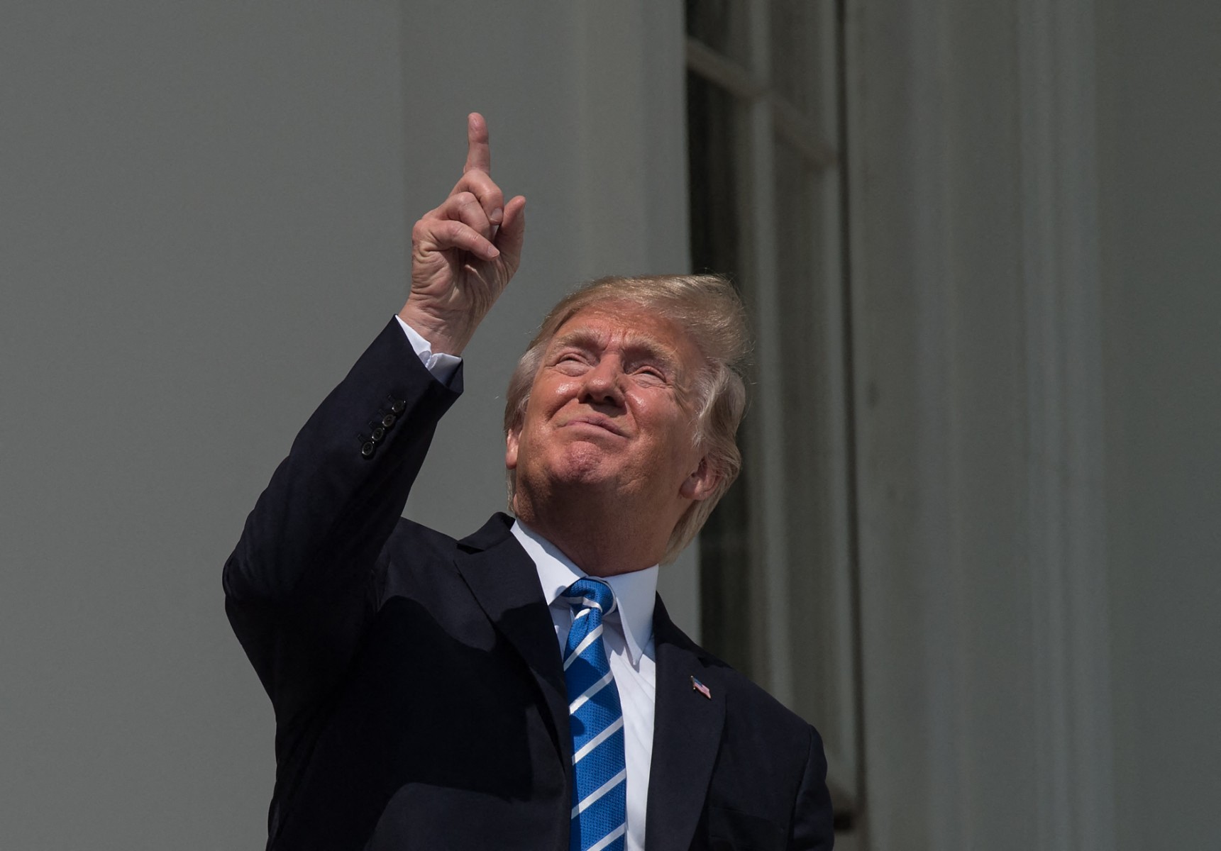 Trump points at the sky and squints at the sun.