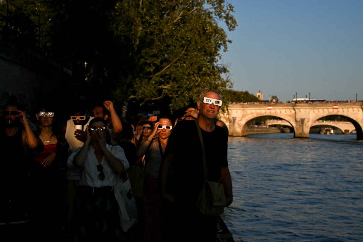 Attendees watch using solar eclipse viewing glasses during a partial solar eclipse along the Seine river banks in Paris
