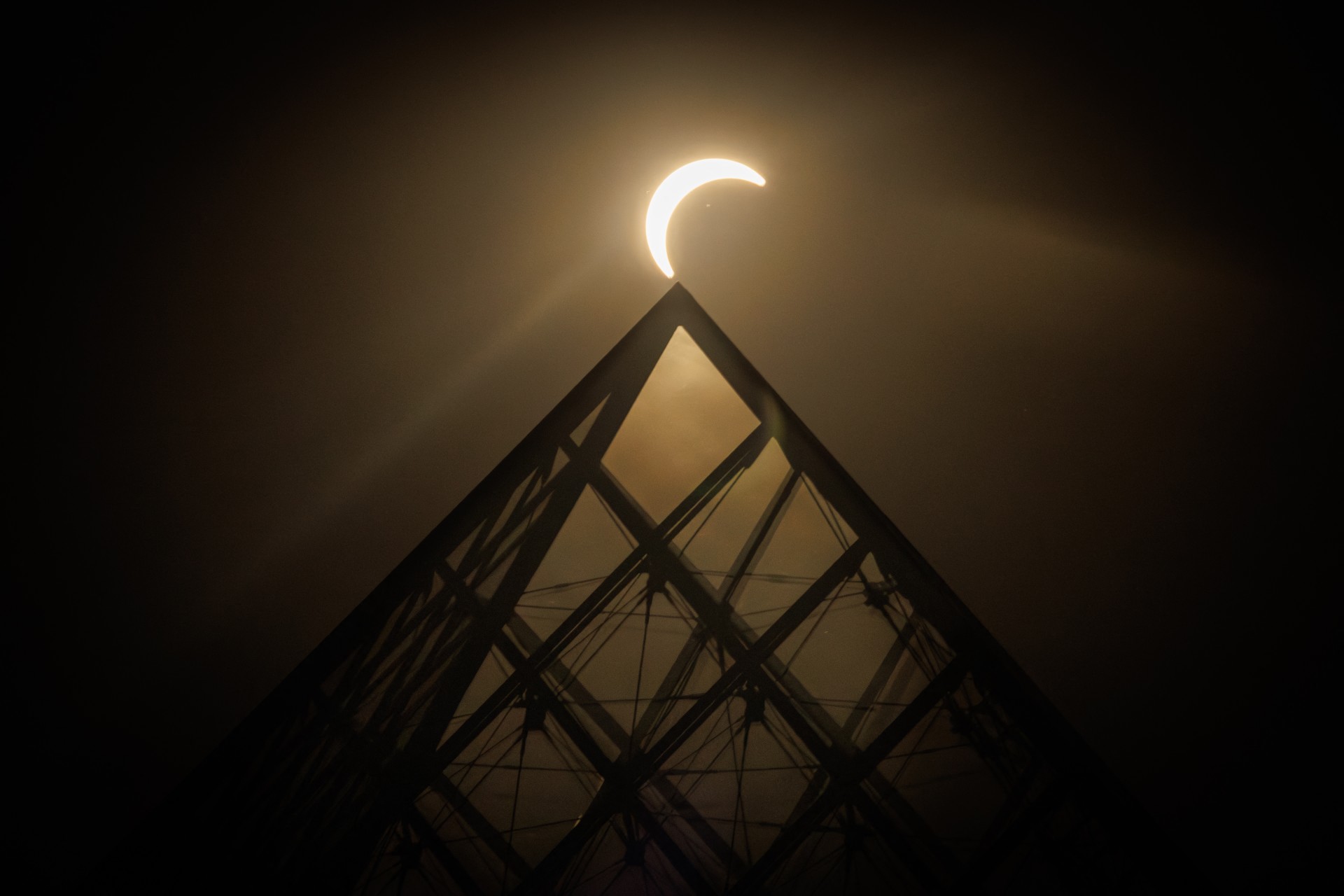 The moon passes over the sun's horizon behind the Pyramide du Louvre