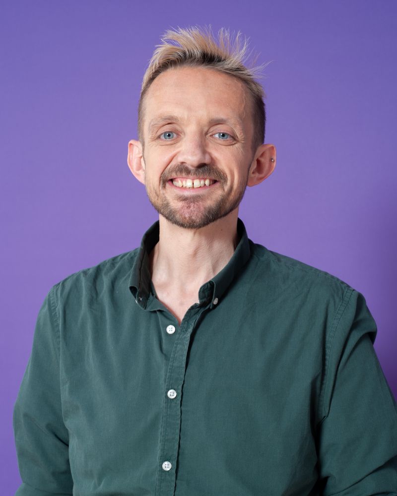 Matt Bristow smiles in front of a purple background.