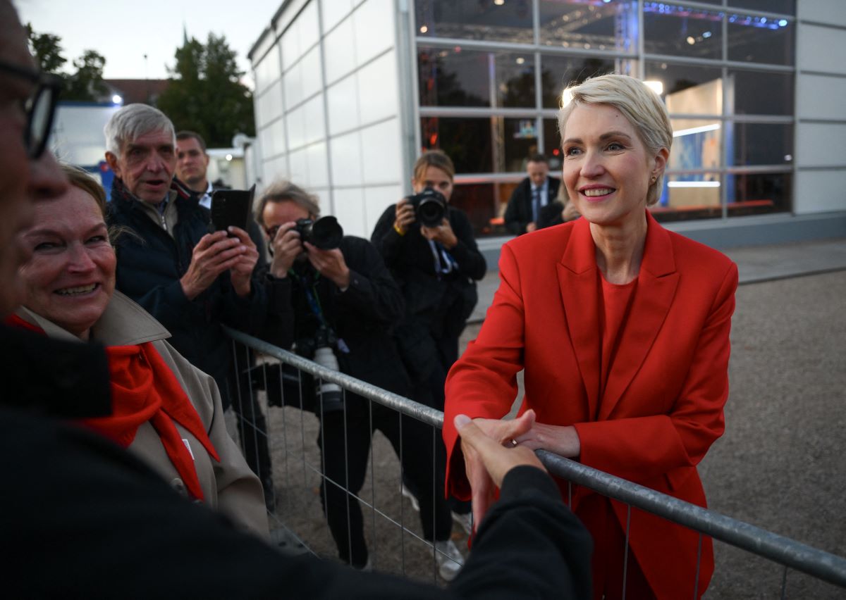 A woman dressed in red shakes hands with someone across a barrier