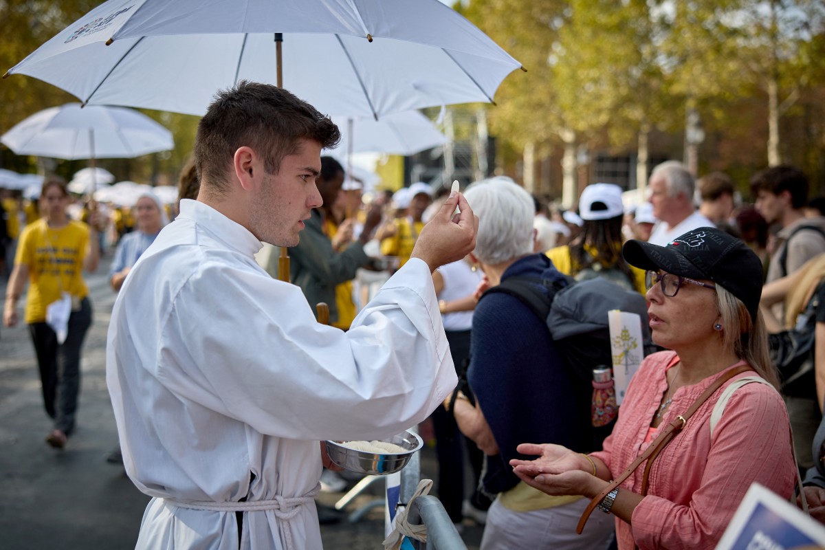 A member of the clergy distributes blessed hosts to worshippers for the communion during a solemn outdoor mass celebrated by Pope Leo XIV at Place de la Concorde, central Paris
