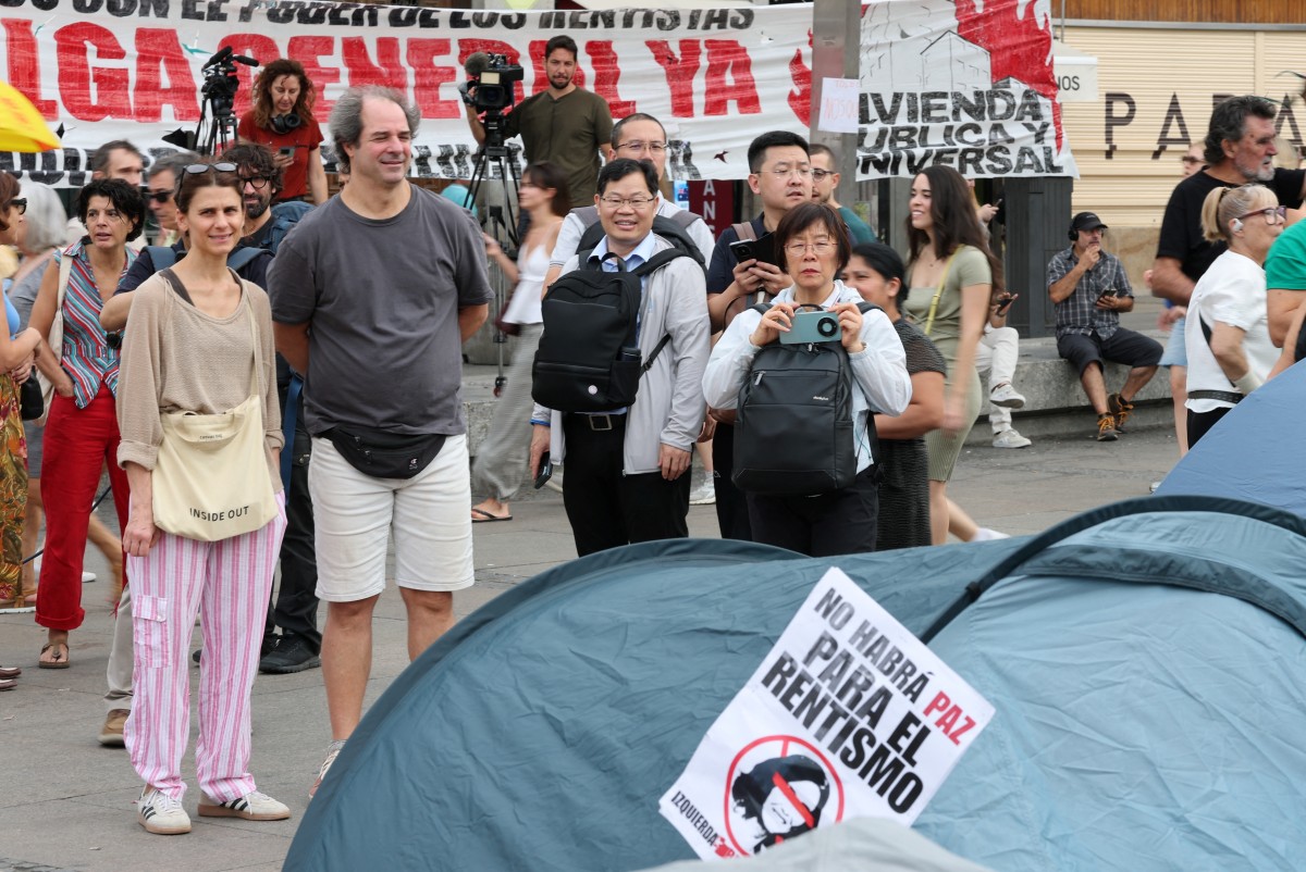 Tourists take pictures as demonstrators camp with tents to protest against evictions and the housing crisis in front of the Presidency of the Community of Madrid on the Puerta del Sol plaza in Madrid