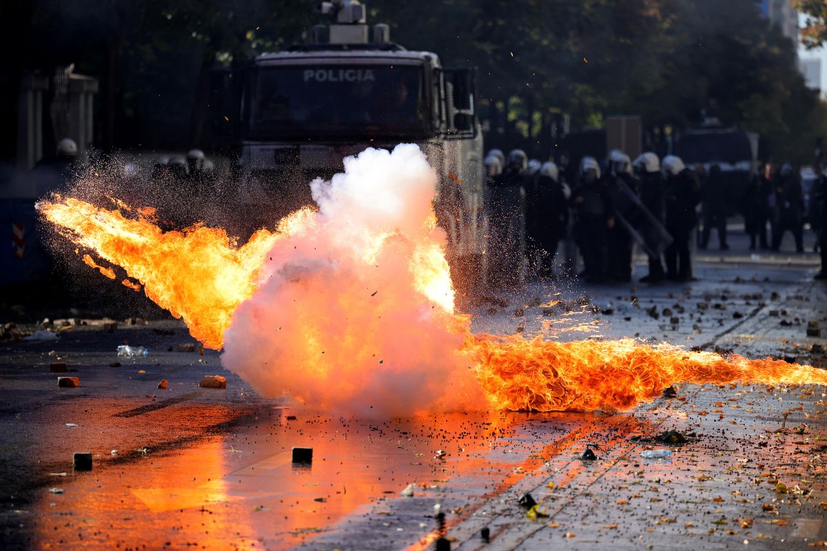 A explosion is seen in front of a squad of police in riot gear in the background.