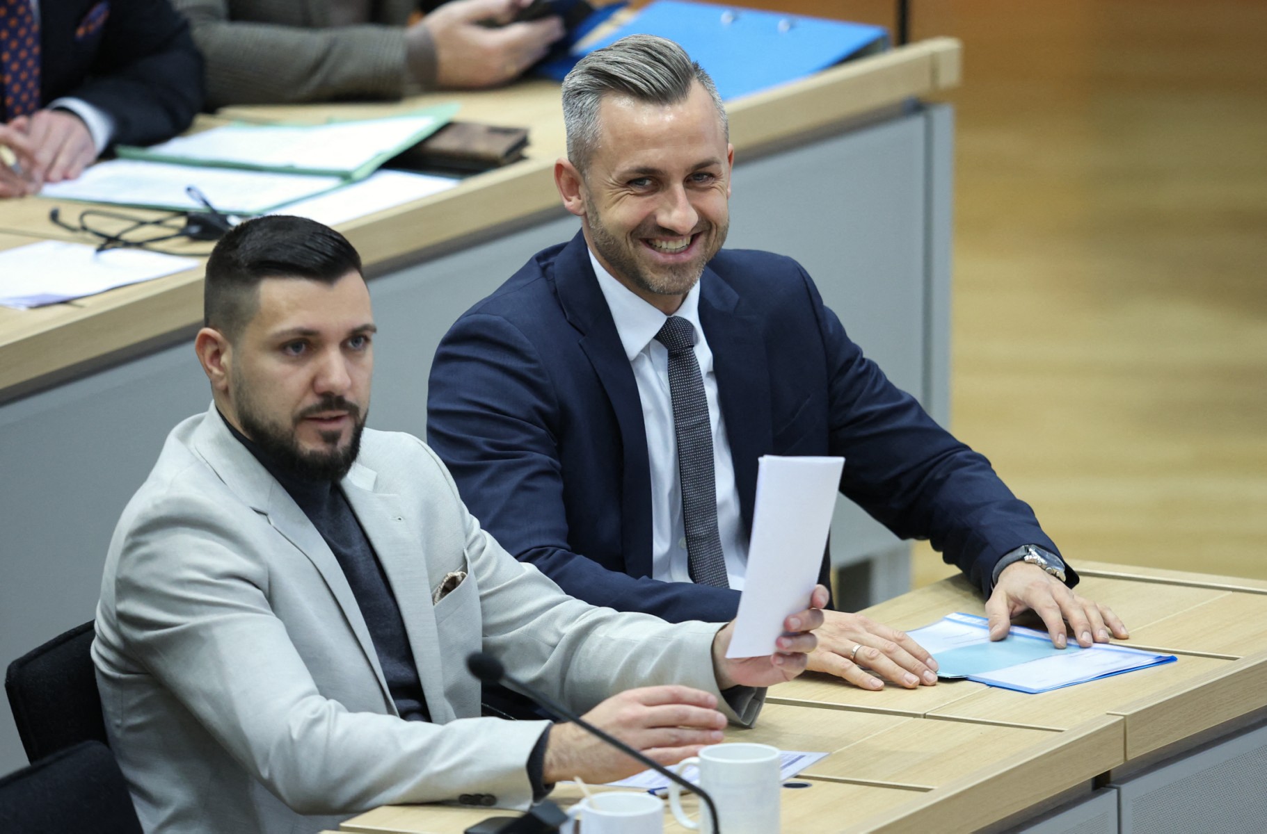 Tobias Rausch in a grey suit sits beside a smiling Ulrich Siegmund.