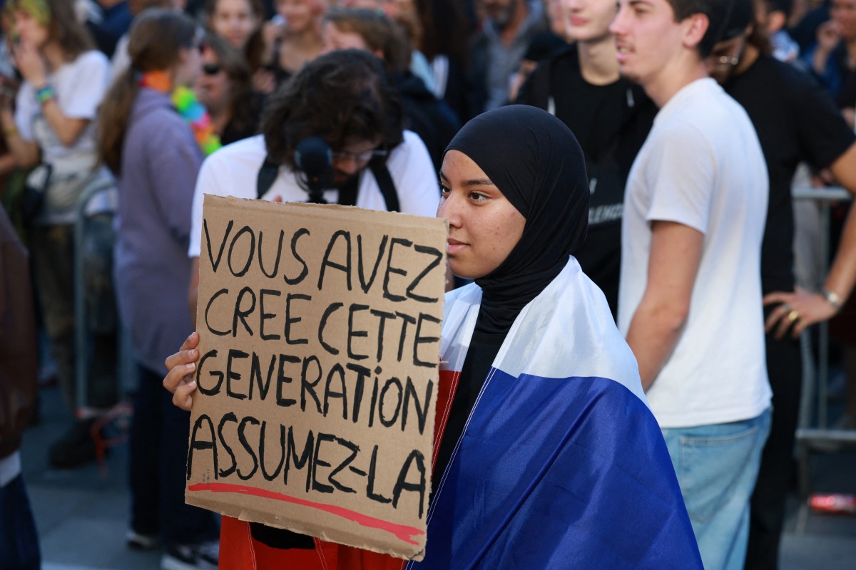 A high school student, wrapped in a flag of France, holds a placard which reads as 'You created this generation, own it' during a gathering amid a nationwide protest movement over school conditions in Saint-Denis, north of Paris