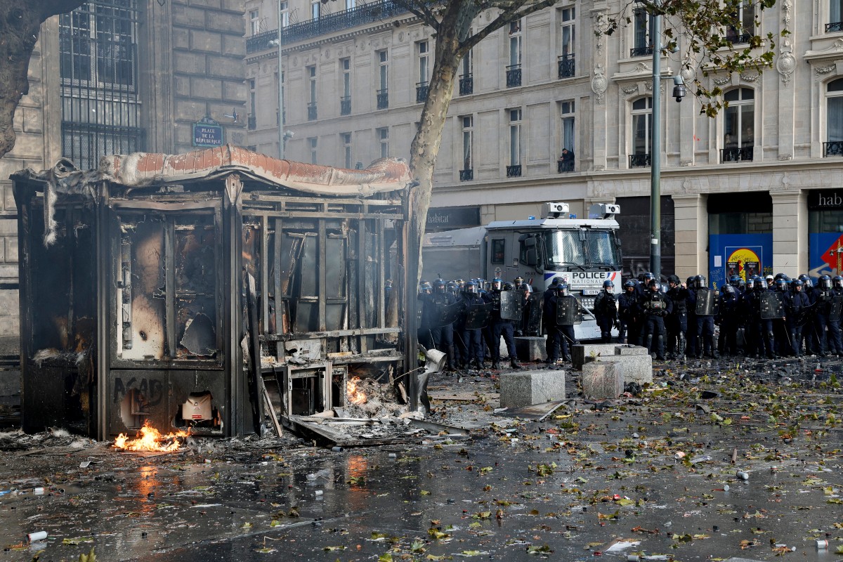 Police officers stand guard past a burnt kiosk on Place de la Republique during a demonstration to protest against the "high cost of living", in Paris 