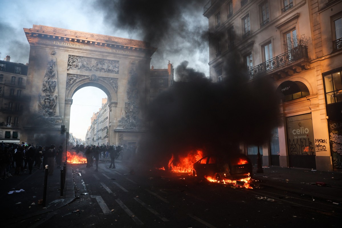 Protestors next to a car on fire near the Porte Saint-Denis during a demonstration to protest against the "high cost of living", in Paris 